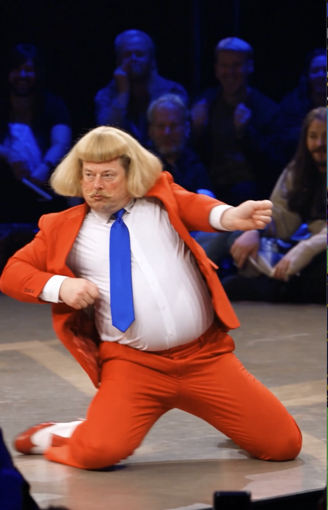 Bobby Bangs in his red suit and blue tie, striking a pose on stage